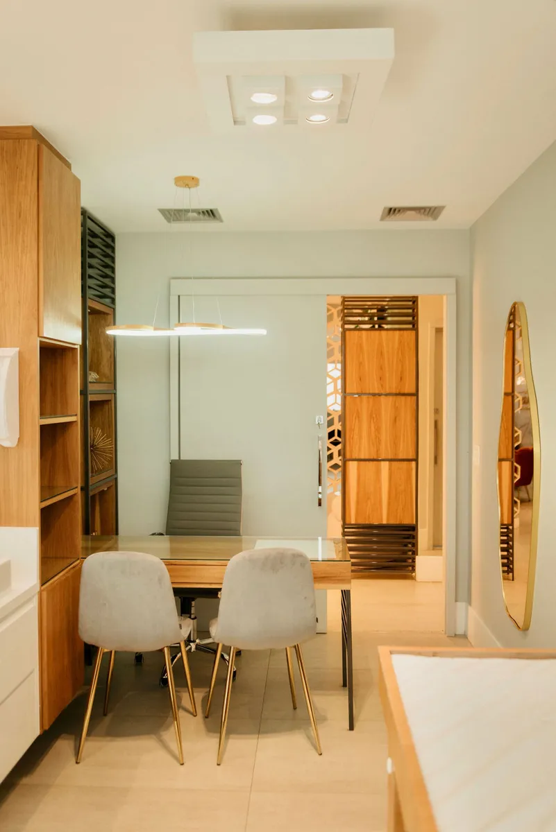 Sala 1: mesa de atendimento em madeira, maca e espelho com moldura dourada
